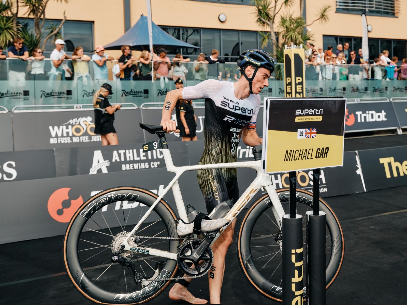 Michael Gar at his bike rack beside his name board at supertri Jersey
